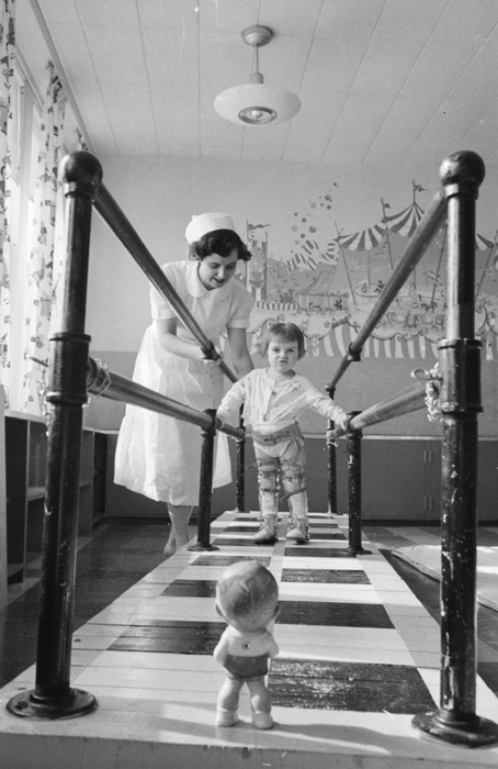 Chris Lund, Mrs. E. Marr, physiotherapist, with Gifford, 2 1⁄2 years old, at the walking bars in the polio clinic at the Sudbury General Hospital, March 1953
